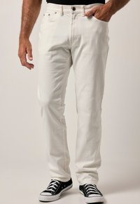 Pantalones de mezclilla blancos de corte recto, con cierre de botón y cremallera, bolsillos frontales y un acabado texturizado sutil, combinados con zapatillas negras.