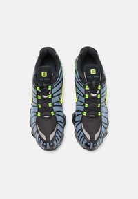 Ténis Nike Shox em azul e preto, com tecido em malha, pormenores em borracha, detalhes em verde e um design de sola chunky distinto.