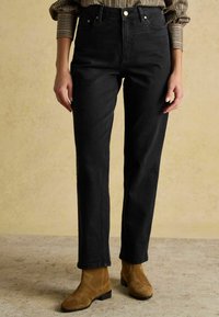 Čierne džínsy z denimu s vysokým pásom a rovnými nohavicami, s piatimi vreckami a zlatými kovovými doplnkami, skombinované s hnedými semišovými členkovými čižmami.