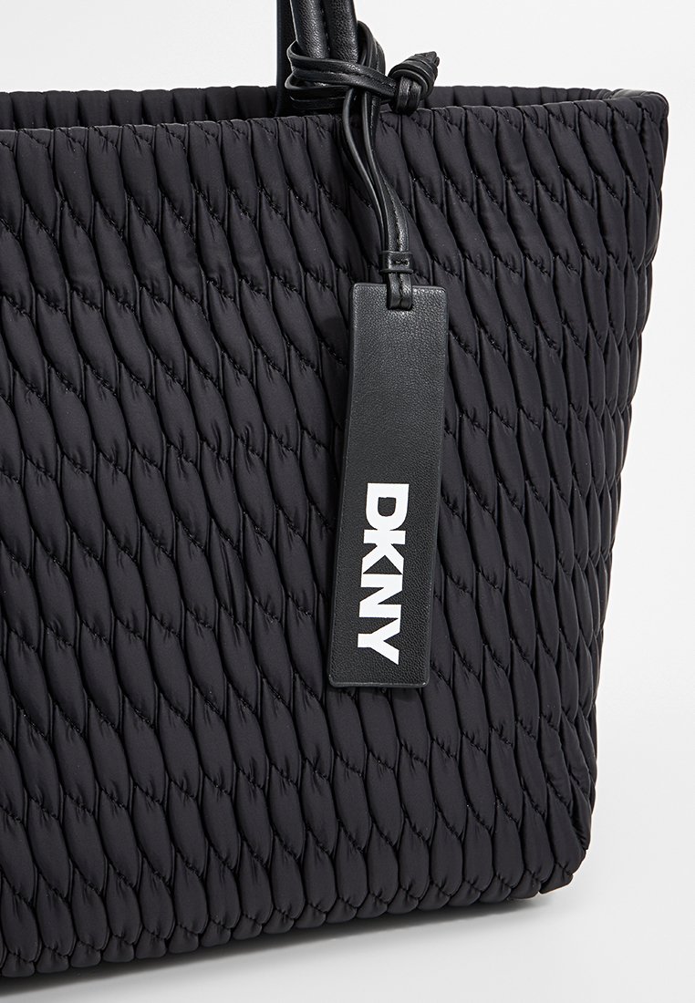Schwarze gesteppte Tragetasche aus Nylon mit einem glatten Lederanhänger mit "DKNY"-Branding. Das Design hat eine strukturierte, gewebte Optik.