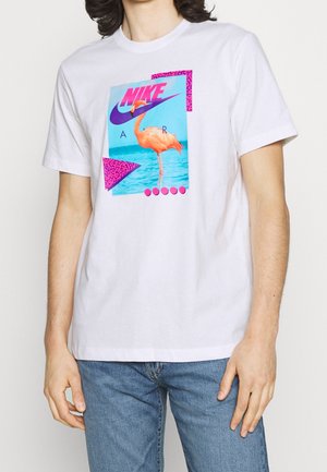 Camiseta blanca de algodón con un estampado gráfico que presenta un flamenco y patrones geométricos en púrpura y rosa. Diseño de mangas cortas y cuello redondo.