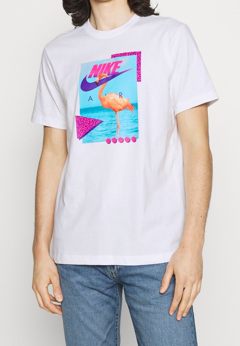 Vit bomull t-shirt med grafisk tryck av en flamingo och geometriska mönster i lila och rosa. Kort ärm och rund halsdesign.