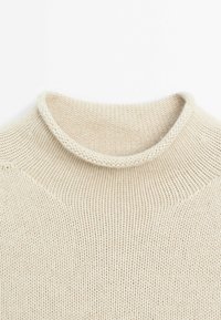 Pull en maille couleur crème avec un col rond légèrement roulé et un motif de points texturé visible.