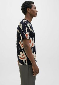 Tamsiai mėlynas trumpų rankovių marškinėliai su dideliu gėlių raštu kremine, koraline ir žalia spalvomis. Minkšta medžiaga, laisvas kirpimas ir šoninės skeltukai.