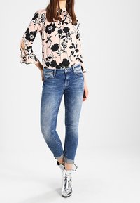 Blusa rosa a fantasia floreale con maniche a taglio, abbinata a jeans skinny blu e stivali alla caviglia argento metallizzati.