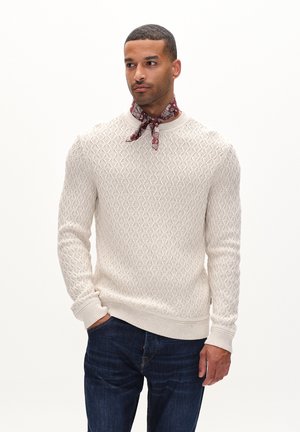 Knit sweater in off-white with textured diamond pattern, ribbed crew neck and cuffs; paired with a patterned burgundy scarf and dark jeans.
