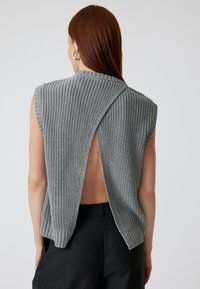 Top grigio senza maniche in maglia con un motivo texturizzato e design con schiena aperta, caratterizzato da un colletto alto e ampie aperture per le braccia.