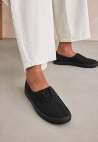 Sorte snøresko i blonder med tekstiloverdel, rundet tå og gummisål. Har øjle detaljer og elastisk åbning for nem påtagning.