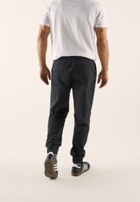 Dark navy joggers with elastic cuffs, elastic waistband, and a smooth texture, paired with black sneakers featuring white stripes.