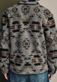 Fleecejacke mit einem abstrakten Muster in Grau, Braun und Schwarz; verfügt über einen Kragen und dickes, strukturiertes Gewebe für Wärme.