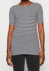 Czarny i biały pasiasty t-shirt z krótkim rękawem i okrągłym dekoltem, wykonany z miękkiej, elastycznej tkaniny. Dodatkowe szczegóły obejmują lekko zaokrąglony dół.