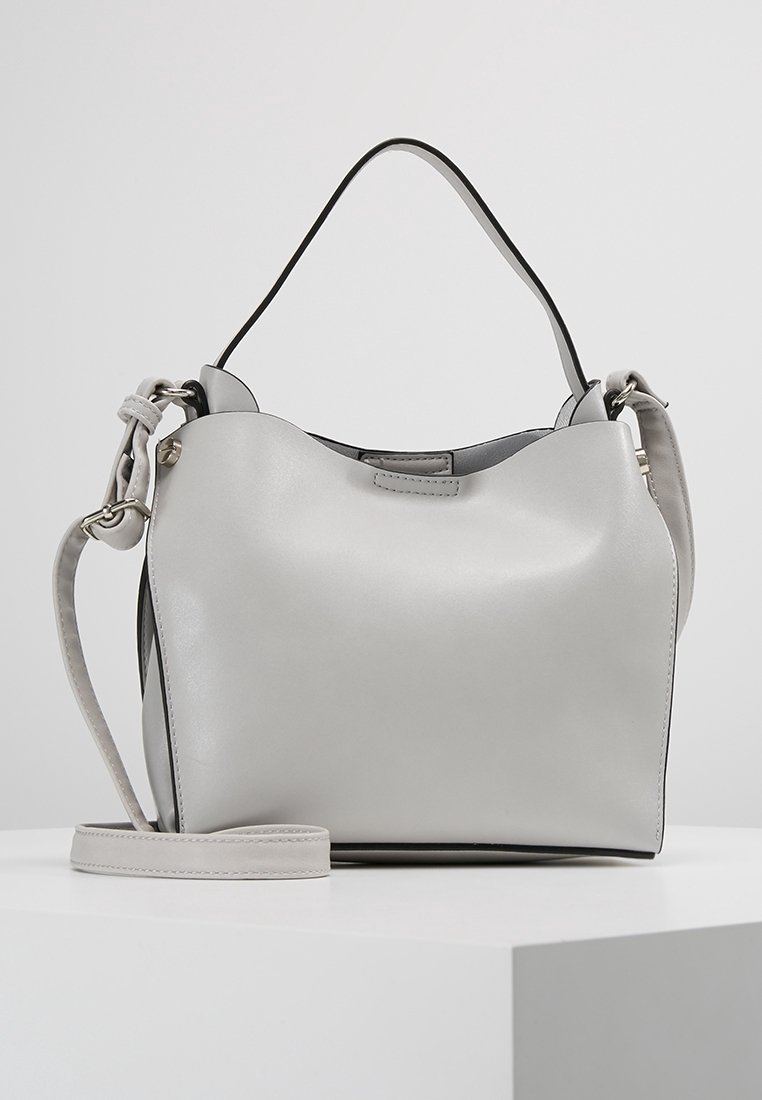 Sac à main en cuir gris clair avec poignée courte et bandoulière longue amovible sur un socle blanc d’exposition.