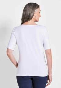 Witte top met korte mouwen en een ronde rug, gemaakt van een gladde stof, gecombineerd met marineblauwe broek. Eenvoudig ontwerp, zonder patronen of accenten.