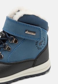 Botte de randonnée bleue et noire avec une tige en Gore-Tex imperméable, un col en fourrure, des œillets en métal et des surpiqûres contrastées.