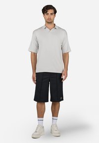 Polo de manga curta cinza claro combinado com calções pretos até ao joelho. Os calções têm um bolso com pala e costuras em contraste. Schners brancas completam o visual.