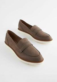 Mocassini in suede marrone con una cinturino perforato, suola in gomma bianca, punta arrotondata e dettagli di cucitura sottili.