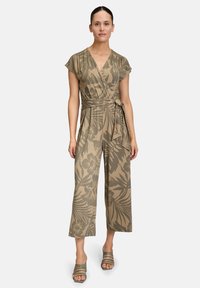 Une combinaison khaki avec un design enveloppé, des manches courtes et un motif floral. Présente une taille nouée et une silhouette à jambes larges. Associée à des talons rayés.