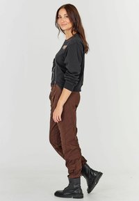 Felpa nera con design grafico, abbinata a pantaloni marroni trapuntati e stivali neri con lacci. L'outfit presenta una vestibilità rilassata e materiali testurizzati.