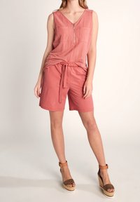 Haut sans manches de couleur rose avec un décolleté en V et deux poches avant, associé à un short assorti noué à la taille, porté avec des sandales à plateforme.