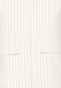 Druskos spalvos švarkas su tamsiai mėlynomis vertikaliomis juostelėmis. Turi du priekinės kišenes bei švelnios audinio tekstūros, atspindinčios pritaikytą dizainą.