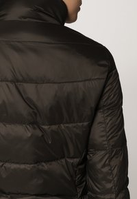 Svart vadderad jacka med hög krage, kviltad textur och horisontella sömdetaljer på baksidan. Snyggt och slätt material.