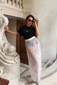 Top de manga corta negro, falda blanca de encaje transparente y gafas de sol. La falda presenta intrincados patrones florales y un diseño de cintura alta.