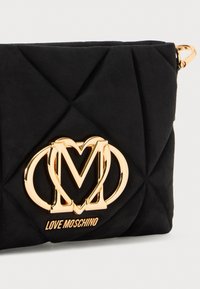 Must have mustriseltkott mustrisest kangast, millel on kuldne Love Moschino logo. Kompaktne ristkülikukujuline disain, siidise lukuga ja õhuke profiil.