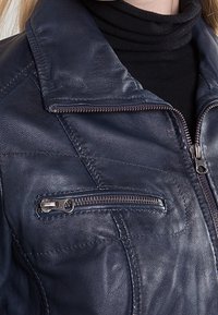 Mörkblå läderjacka med dragkedja framtill, diskreta sömdetaljer och en bröstficka med en silverfärgad dragkedja. Texturerad yta.