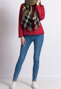 Veste rembourrée rouge, écharpe écossaise verte avec des franges, jeans skinny bleus et baskets blanches. Design simple avec des textures lisses et des couleurs contrastées.