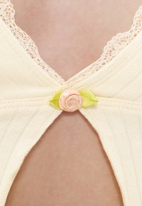 Gros plan de tissu côtelé crème avec un galon en dentelle et une petite rose rose avec des feuilles vertes à l’ouverture de la couture centrale.