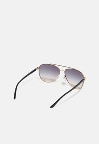 Flieger-Sonnenbrille mit einem Rahmen aus roségoldnem Metall, grau verlaufenden Gläsern und schwarzen Kunststoffbügeln. Verfügt über verstellbare Nasenpolster.