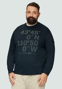 Sweat-shirt bleu marine en mélange de coton avec un grand graphique comprenant des coordonnées et des logos. Il a un col ras du cou et des poignets côtelés. Design minimaliste.