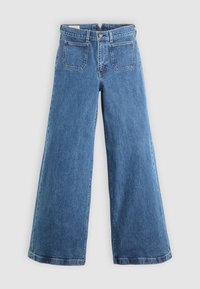 Jean en denim bleu à jambes larges avec poches avant, passants de ceinture, fermeture à boutons et coutures visibles sur un fond clair uni.