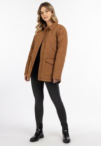 Bruine gewatteerde jas met een knoopsluiting, kraag en voorzak; gecombineerd met zwarte skinny jeans en zwarte enkellaarsjes.