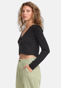 Black cropped cardigan with a deep V-neck, long sleeves, and a textured pattern, paired with light green corduroy pants.
