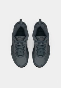 Egy sötétszürke Nike Air Monarch sneakerpár, felülnézetből, fehér háttéren, fűzős és tiszta állapotban.