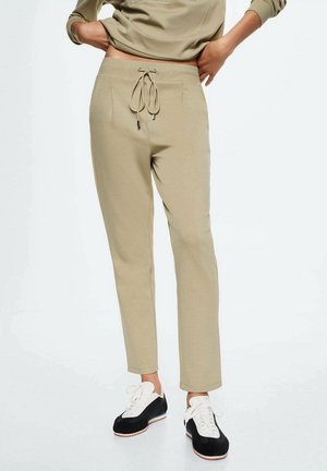 Pantalones beige de pierna recta con cintura ajustable con cordón, usados con zapatillas negras y blancas de cordones, vistos desde la cintura hasta los tobillos.