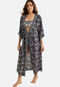 Zwarte doorzichtige kimono met witte en oranje bloempatronen, open voorkant, wijde mouwen en een strik taille. Bevat een bijpassende bandeau met patroon eronder.