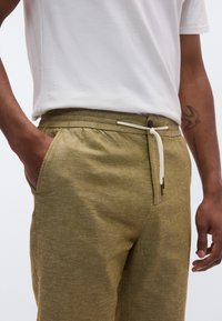 Παντελόνι από πράσινο λινό με ελαστική μέση, κορδόνι σύσφιξης και πλαϊνές τσέπες. Κανονική εφαρμογή με υφή στην επιφάνεια.