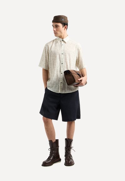 Camicia con bottoni realizzata in un tessuto leggero e stampato. Abbinata a pantaloni corti scuri e stivali in pelle marrone. Tiene una borsa marrone.