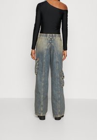 Mustat yhdelle olalle menevä bodysuit, joka on yhdistetty sinisiin, löysiin cargo-farkkuihin, joissa on kaksinkertaiset sivutaskut ja teksturoitu denim-pinta.