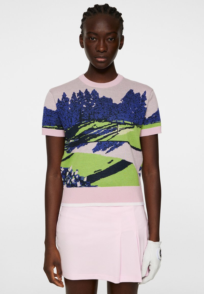 Sweter golfowy z dzianiny w pastelowym różu z wielokolorowym wzorem krajobrazowym przedstawiającym drzewa i wzgórza. Krótkie rękawy i detal z ribbingiem przy kołnierzu.