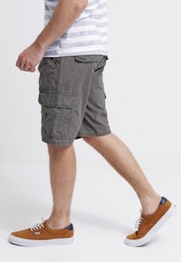 Pantaloni cargo grigi con moltetasche, realizzati in materiale di cotone. Abbinati a scarpe marroni con accenti blu navy e suole bianche.