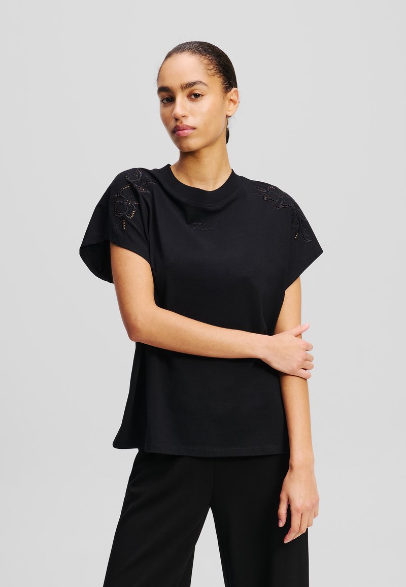 Black short-sleeve t-shirt with floral embroidery on shoulders, round neckline, and relaxed fit. Made from soft cotton material.