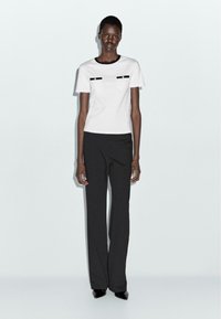 White short-sleeved t-shirt with black pocket accents paired with black wide-leg trousers. Smooth fabric and fitted silhouette. Black high heels.