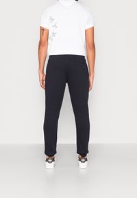 Zwarte joggers van zachte stof, slim-fit ontwerp, met een achterzak en gedragen met witte sneakers en een wit T-shirt.