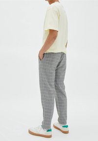 T-shirt di cotone gialla, slim fit; pantaloni a quadri grigi con tasche; sneaker bianche con accenti verdi e suole marrone chiaro.