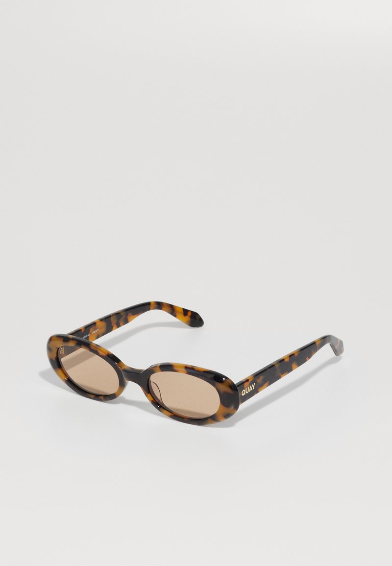 Óculos de sol de tartaruga com lentes ovais e tonalidade castanha. Apresentam armações curvadas e marcação elevada no braço. Textura de plástico suave.