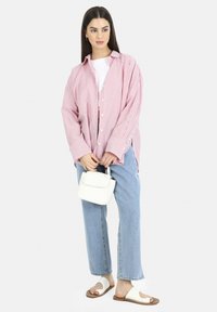 Camisa de rayas rojas y blancas de gran tamaño, camiseta blanca debajo, jeans de un azul claro, bolsa tejida blanca y sandalias beige de diseño abierto en la punta.