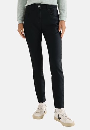 Svarta jeans med slim fit, som har en klassisk femfickdesign, kontrasterande sömmar och bärs med vita sneakers.